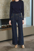 Person wearing a navy sweater and wide-leg jeans standing in a room with a stone wall.