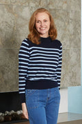 Woman wearing a navy and white striped sweater and blue jeans standing against a stone wall.
