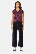 Woman wearing a sleeveless patterned top and black pants on a white background