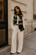 Woman wearing a white coat and plaid scarf standing on a city street.