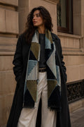 Woman wearing a long coat and patterned scarf standing against a stone building.