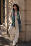 Woman wearing a colorful scarf and white outfit leaning against a building.
