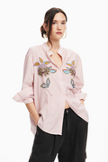 Woman wearing a pink striped shirt with colorful floral embroidery on a white background