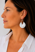 A close-up side profile of a woman wearing a textured silver dangle earring with a scalloped, fan-like design.