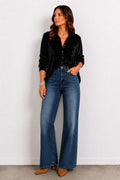 Woman wearing a black satin shirt and blue jeans against a white background
