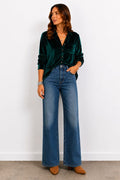 Woman wearing a green velvet shirt and blue jeans against a white background
