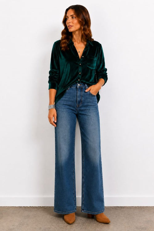 Woman wearing a green velvet shirt and blue jeans against a white background