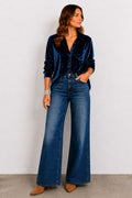 Woman wearing a blue velvet shirt and wide-leg jeans against a white background