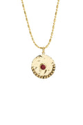A gold-tone necklace featuring a textured circular pendant with a small red gemstone in the center and a beaded border, shown against a plain white background.