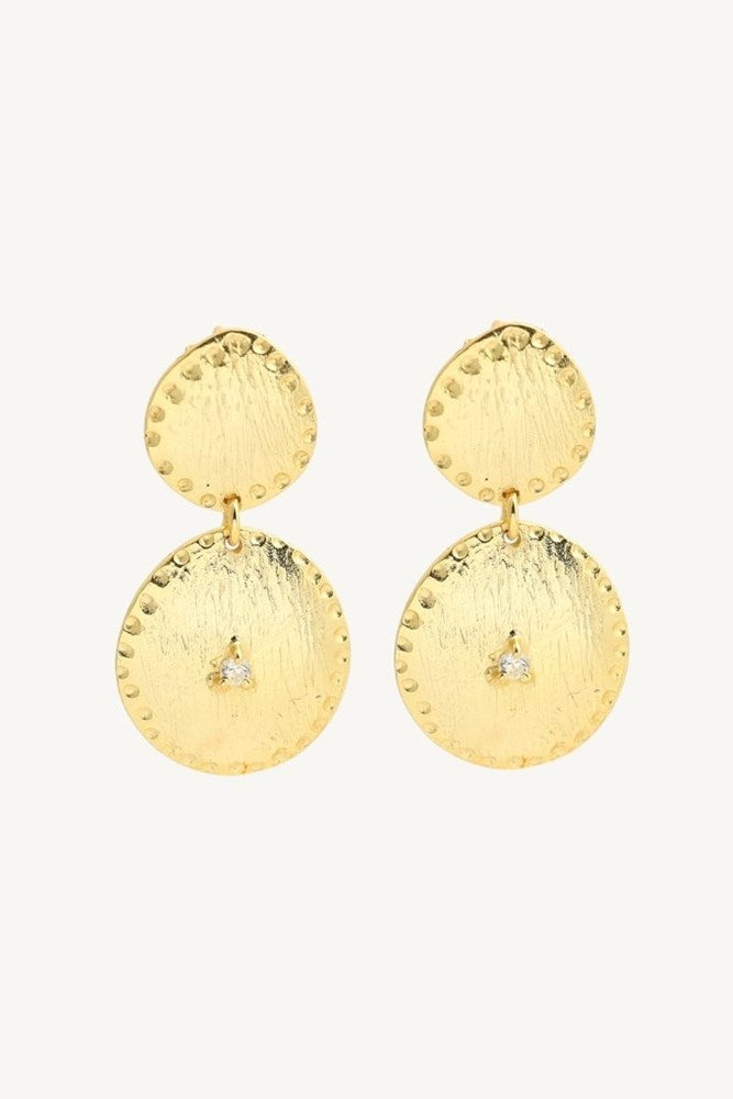 A pair of textured gold drop earrings with a small clear crystal accent on the lower disc, shown against a plain off-white background