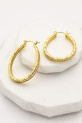 A pair of gold hoop earrings with a row of small clear stones along the front, displayed on a white marble pedestal against a white background.