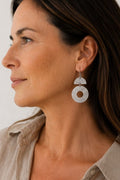 A close-up side profile of a woman wearing a textured silver dangle earring with a semi-circle and circular design.