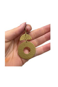 A hand holding a pair of hammered gold-tone earrings, featuring a large circular disc earring with a center cutout and a smaller semi-circular disc charm.