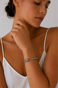 A close-up lifestyle shot of a woman wearing a silver-toned snake bracelet on her wrist, paired with a white camisole top against a neutral light gray background.