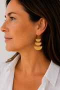 A close-up side profile of a woman wearing a pair of gold-toned dangle earrings with three stacked textured semicircle shapes.