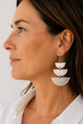 A close-up side profile of a woman wearing a pair of silver drop earrings with three stacked hammered semicircle charms.