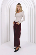 Woman wearing a beige top and burgundy pants in a white geometric background