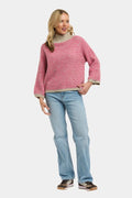 A woman modeling a pink and white patterned knit sweater with a beige turtleneck collar and cuffs, paired with light blue jeans and brown shoes, against a light gray background.