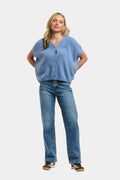 A woman modeling a light blue knit cardigan with short dolman sleeves and a button front, paired with blue jeans and dark sneakers, against a plain light gray background.