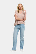 A woman modeling a light pink short-sleeve button-up top and light blue straight-leg jeans against a plain light gray background.