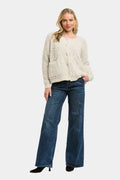 A woman modeling a cream-colored, textured knit cardigan sweater paired with wide-leg blue jeans and black heels, set against a plain light gray background.