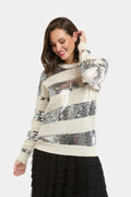 A woman wearing a cream and silver sequined striped sweater with a black ruffled skirt, posing against a light gray studio background.