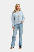 A woman modeling a light blue and white striped knit cardigan sweater with a beige button placket, paired with light-wash blue jeans, against a plain light gray background.