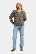 A woman modeling a brown and black striped knit cardigan with a pink zipper and trim, paired with light blue jeans and dark sneakers, against a light gray background.
