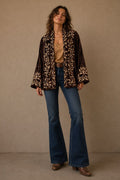 Woman wearing a patterned blouse and blue jeans against a beige background