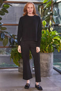 Woman in black outfit standing in a modern indoor setting with plants.